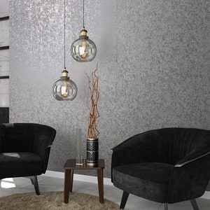 Op de afbeelding: Twee zwarte fauteuils met gouden accenten staan in een kamer met een getextureerde grijze muur. Twee glazen globe-hanglampen hangen aan het plafond. Een kleine houten tafel met een vaas met gedroogde takken staat tussen de fauteuils.