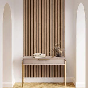Peut inclure: Une entrée moderne avec une console rose clair à pieds dorés, deux tiroirs et un mur à lattes de bois. La table contient des livres et un vase avec des fleurs séchées. Le sol est un motif de chevrons en bois clair.