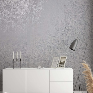 Op de afbeelding: Een witte kast met twee deuren en twee lades staat op een houten vloer voor een grijze, getextureerde muur. Een zwarte kaarsenhouder met drie kaarsen staat op de kast. Twee ingelijste foto's en een paar zilveren ornamenten staan ook op de kast. Een zwarte staande lamp met een witte verenpluim staat in de hoek van de kamer.