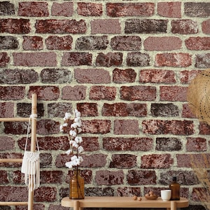 Può includere: Un muro di mattoni con mattoni rossi e marroni variabili, con malta beige chiaro. Una scala di legno, un piccolo vaso con fiori bianchi e un tavolino con oggetti decorativi sono in primo piano. Il muro ha un'estetica rustica e vintage.