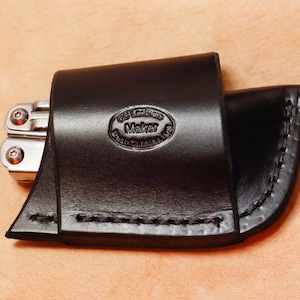 Peut inclure: Étui en cuir noir pour multi-outils avec un bord cousu et un logo "GG Leather Maker" en relief.
