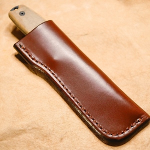 May include: A brown leather knife sheath with a stitched edge.