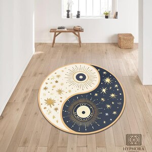 Peut inclure: Tapis rond avec un motif yin-yang. Un côté est crème avec des étoiles dorées et un œil en forme d'éclat de soleil, l'autre est bleu marine avec des étoiles dorées et un œil en forme d'éclat de soleil. Le tapis est sur un parquet.