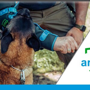 Pu&ograve; includere: Una persona che indossa protezioni per le braccia con il testo "Dog Armour Pro" sul proteggi-braccio sinistro, sta addestrando un cane marrone e nero. Il cane indossa un collare e un guinzaglio argentati. La persona indossa una camicia verde e pantaloni kaki. Lo sfondo &egrave; un'area erbosa verde.