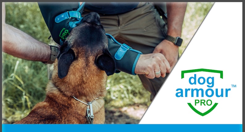 Pu&ograve; includere: Una persona che indossa protezioni per le braccia con il testo "Dog Armour Pro" sul proteggi-braccio sinistro, sta addestrando un cane marrone e nero. Il cane indossa un collare e un guinzaglio argentati. La persona indossa una camicia verde e pantaloni kaki. Lo sfondo &egrave; un'area erbosa verde.