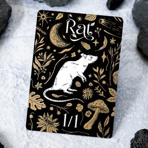 May include: A black card with gold illustrations of a white rat, mushrooms, and other botanical elements. The card has the word "Rat" in gold lettering and the number "1/1" in white lettering.