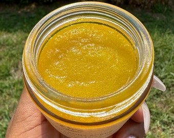 Può includere: Primo piano di un barattolo di vetro pieno di uno scrub corporeo giallo brillante e granuloso. Lo scrub ha un aspetto lucido e umido.