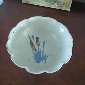 May include: A white ceramic bowl with a scalloped rim and a blue and brown floral design. The bowl has a speckled glaze.