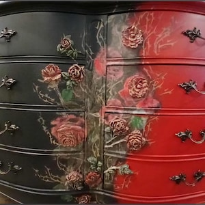 May include: A two-toned dresser with a black and red finish. The black side features rose and thorn accents, while the red side has rose embellishments. Each drawer has ornate, dark metal handles.