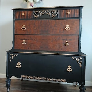May include: A black and gold dresser with five drawers and ornate details. The dresser has a dark wood top and gold accents on the drawers and legs.