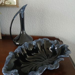 May include: A black ceramic leaf-shaped bowl and a tall, slender vase with a curved handle. The bowl has a glossy finish with a blue-grey trim. The vase is black with blue-grey accents.