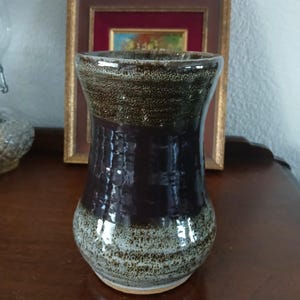 May include: A handcrafted ceramic vase with a dark brown, textured body and a lighter speckled rim. The vase has a flared shape and a glossy finish, suitable for displaying flowers or as a decorative piece. The vase is approximately 7 inches tall.