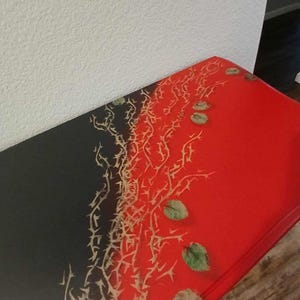 May include: A rectangular table with a striking design. The table's surface is divided into two sections: one black and the other red. A pattern of thorny branches and leaves in shades of beige and green adorns the surface.