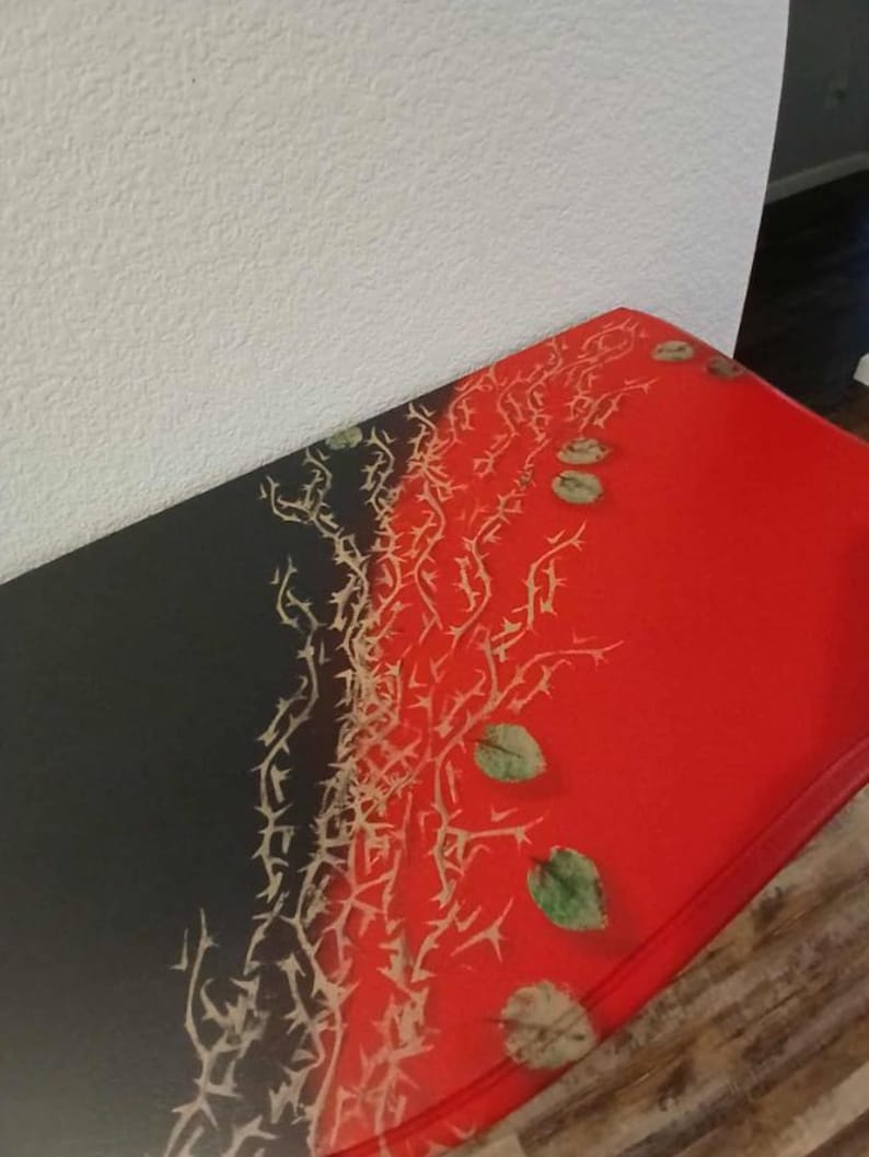 May include: A rectangular table with a striking design. The table's surface is divided into two sections: one black and the other red. A pattern of thorny branches and leaves in shades of beige and green adorns the surface.