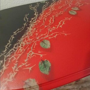 May include: A red, oval-shaped table with a black corner. The table is decorated with a thorn design and green leaf accents. The table is a unique piece of furniture.