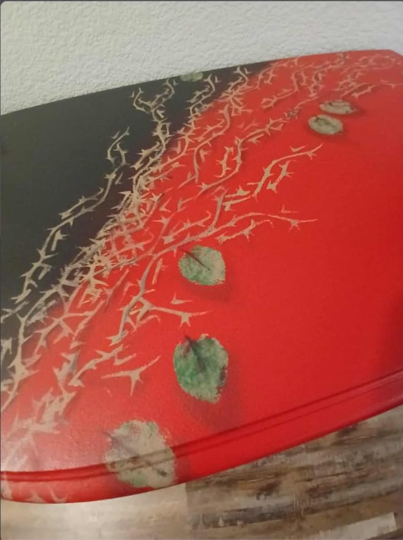 May include: A red, oval-shaped table with a black corner. The table is decorated with a thorn design and green leaf accents. The table is a unique piece of furniture.