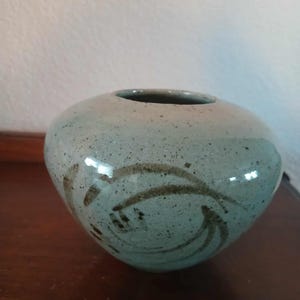 May include: A round, speckled ceramic vase in shades of blue and gray, with a dark brown swirl design. The vase has a wide opening and a smooth, glossy finish. A decorative piece for home decor.