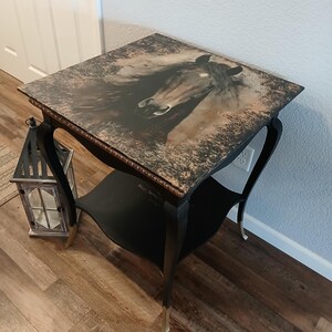May include: A black end table with a distressed finish and gold accents. The top of the table features a printed image of a horse's head.