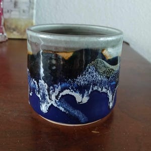 May include: A ceramic mug with a blue, black, and white glaze. The mug has a unique, abstract design.