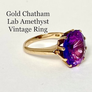 May include: A vintage gold ring with a large, faceted, purple amethyst gemstone. The ring is set in a simple, elegant style.