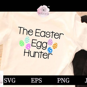 May include: White t-shirt with the text "The Easter Egg Hunter" in black. There are five colorful Easter egg graphics around the text.