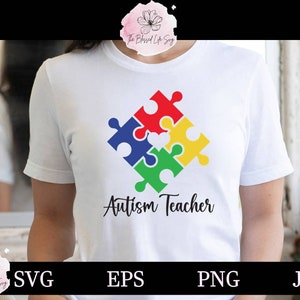 May include: White t-shirt with a colorful puzzle piece design and the text "Autism Teacher" printed on the front.