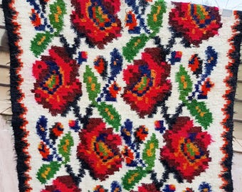 May include: A white rug with a black border and a floral pattern in red, green, blue, and yellow.