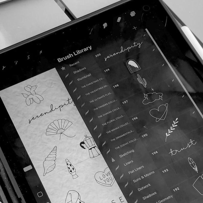 May include: A black and white digital drawing tablet screen displaying a list of brush libraries and icons. The brush libraries include "Shadows", "Thumbnail", "The Christmas Co", "The Valentines Da", "The Ultimate Flash", "The Fingers Colle", "The Chakra Colle", "The Floral Colle", "The Mahas Collec", "The Ornamentals", "The Zodiac Colle", "Sketching", "Liners", "Flat Liners", "Suns & Moons", "Dotwork", "Shadows", and "Geometry". The icons include a balloon animal, a fan, a seashell, a lava lamp, a coffee pot, a heart with the words "Love You", a cactus, a cloud with a heart, a branch with leaves, and a feather.