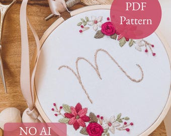 May include: Embroidered hoop art with a floral design and the letter "M". The embroidery features red, pink, and white flowers with green leaves. The text "PDF Pattern" is in a pink circle. The text "NO AI 100% human made" is at the bottom.