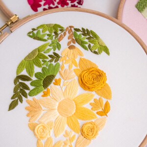 May include: A floral embroidery hoop featuring a lemon design. The lemon is composed of yellow, orange, and green thread, with detailed leaves and flowers. The embroidery is set against a white fabric background, framed by a wooden hoop.