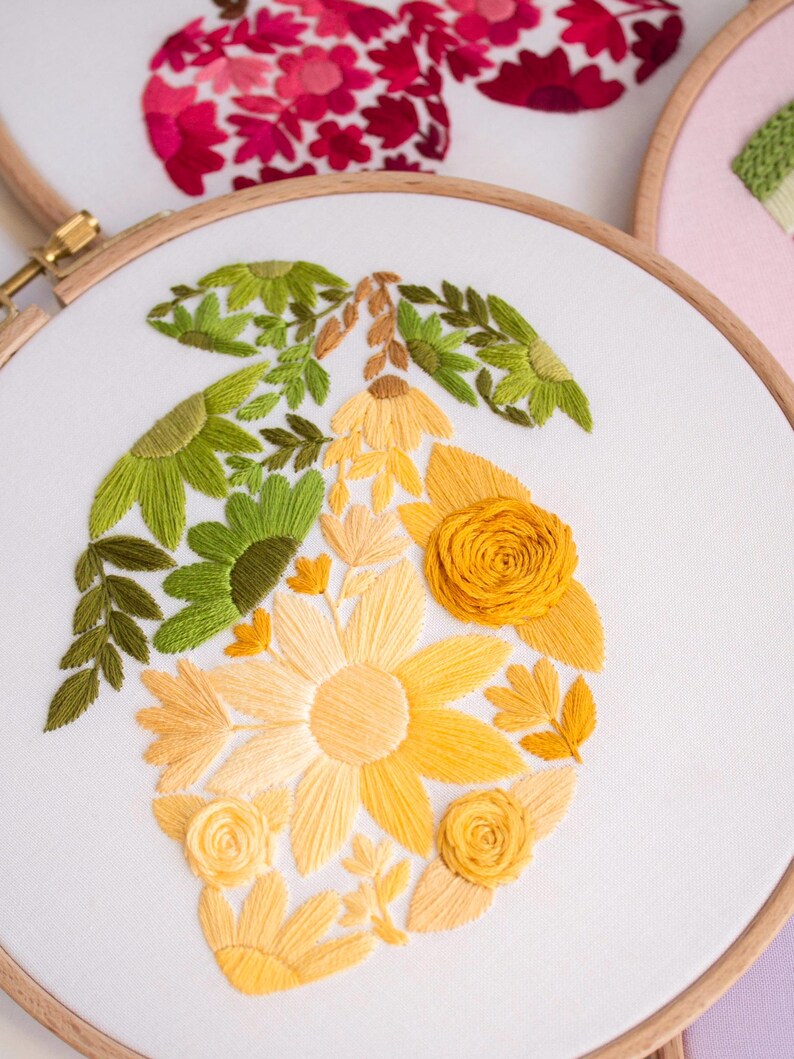 May include: A floral embroidery hoop featuring a lemon design. The lemon is composed of yellow, orange, and green thread, with detailed leaves and flowers. The embroidery is set against a white fabric background, framed by a wooden hoop.