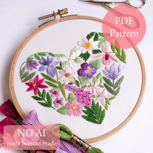 May include: A wooden embroidery hoop containing white fabric with a heart-shaped floral embroidery design featuring various colorful flowers and green leaves. The text PDF Pattern is visible in the top right, and NO AI 100% human made is at the bottom.
