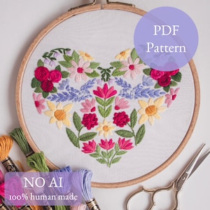 May include: An embroidery hoop with a heart-shaped floral design. The design features red, pink, yellow, and purple flowers with green leaves. The text "PDF Pattern" is in a purple circle. The text "NO AI 100% human made" is also visible.