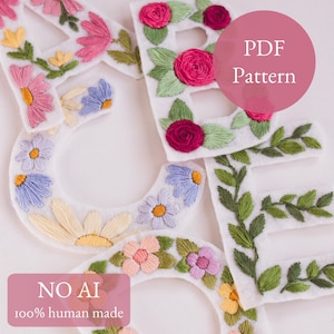 以下が含まれることがあります： ピンク、黄色、青色の花の刺繍が施された、"ACE"の文字を綴る刺繍フェルト文字。文字は白で、手縫いの花と葉が特徴です。画像には「PDF Pattern」と「NO AI 100% human made」というテキストが含まれています。