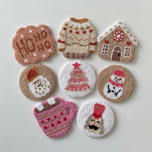 May include: Nine round felt Christmas decorations with various designs, including a snowman, a Christmas tree, a gingerbread house, a Father Christmas, a mug of hot chocolate, a jumper, and a sign that says "Ho Ho Ho".