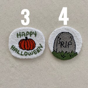 May include: Two handmade Halloween-themed punch needle crafts. The first is a white circle with the words "Happy Halloween" and an orange pumpkin. The second is a white circle with a gray tombstone that says "RIP" and green grass.
