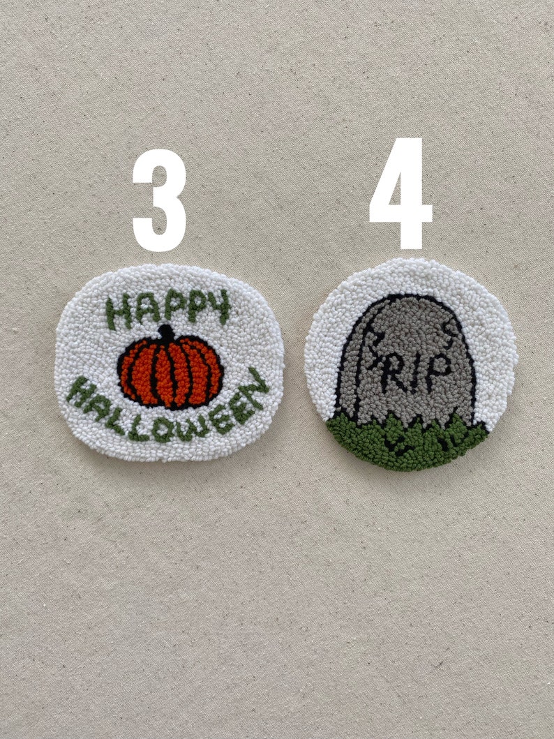 May include: Two handmade Halloween-themed punch needle crafts. The first is a white circle with the words "Happy Halloween" and an orange pumpkin. The second is a white circle with a gray tombstone that says "RIP" and green grass.