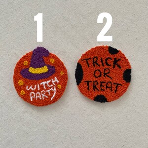 May include: Two orange and black Halloween themed needlepoint ornaments. The first ornament features a purple witch hat with a yellow brim and the text "Witch Party". The second ornament features black polka dots and the text "Trick or Treat".