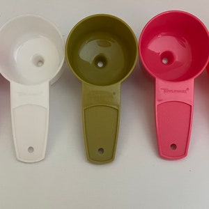 May include: Five plastic funnels in different colours: pink, white, green, red, and orange. The funnels have a wide top and a narrow spout. The funnels are all labelled "Tupperware".