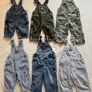 Puede incluir: Seis pares de pantalones de mezclilla azul con tirantes para beb&eacute;s o ni&ntilde;os peque&ntilde;os. Los pantalones de mezclilla son de diferentes estilos, incluyendo rayas, azul s&oacute;lido y camuflaje.