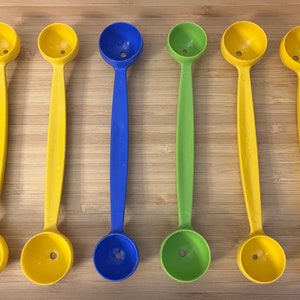May include: Six melon ball scoops in a wooden tray. Two are yellow, two are yellow with a blue handle, one is green with a green handle, and one is blue with a blue handle.