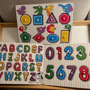 May include: Three wooden puzzle boards with colourful illustrations. The first board has letters A-Z, the second board has numbers 0-9, and the third board has various shapes with animal illustrations.