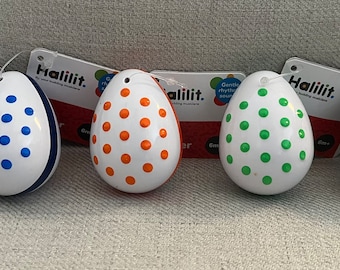 May include: Six colorful egg shakers with white bases and different colored polka dots. The shakers are labeled "Halilit. Egg Shakers 6m+"