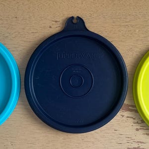 Puede incluir: Tres tapas de plástico para recipientes de almacenamiento en azul, verde y amarillo. Cada tapa tiene un asa y la palabra "Tupperware" impresa en la parte superior.