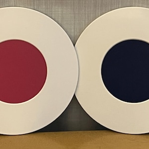 May include: Two white circular coasters with a smaller circle in the center. The coaster on the left has a pink circle in the center and the coaster on the right has a dark blue circle in the center.
