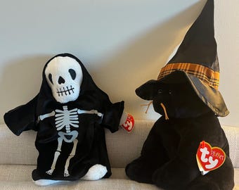 Puede incluir: Dos juguetes de peluche de Halloween. Un gato negro con un sombrero de bruja con ribete de cuadros naranja y negro y un esqueleto con una túnica negra con capucha. Ambos juguetes tienen etiquetas Ty rojas.