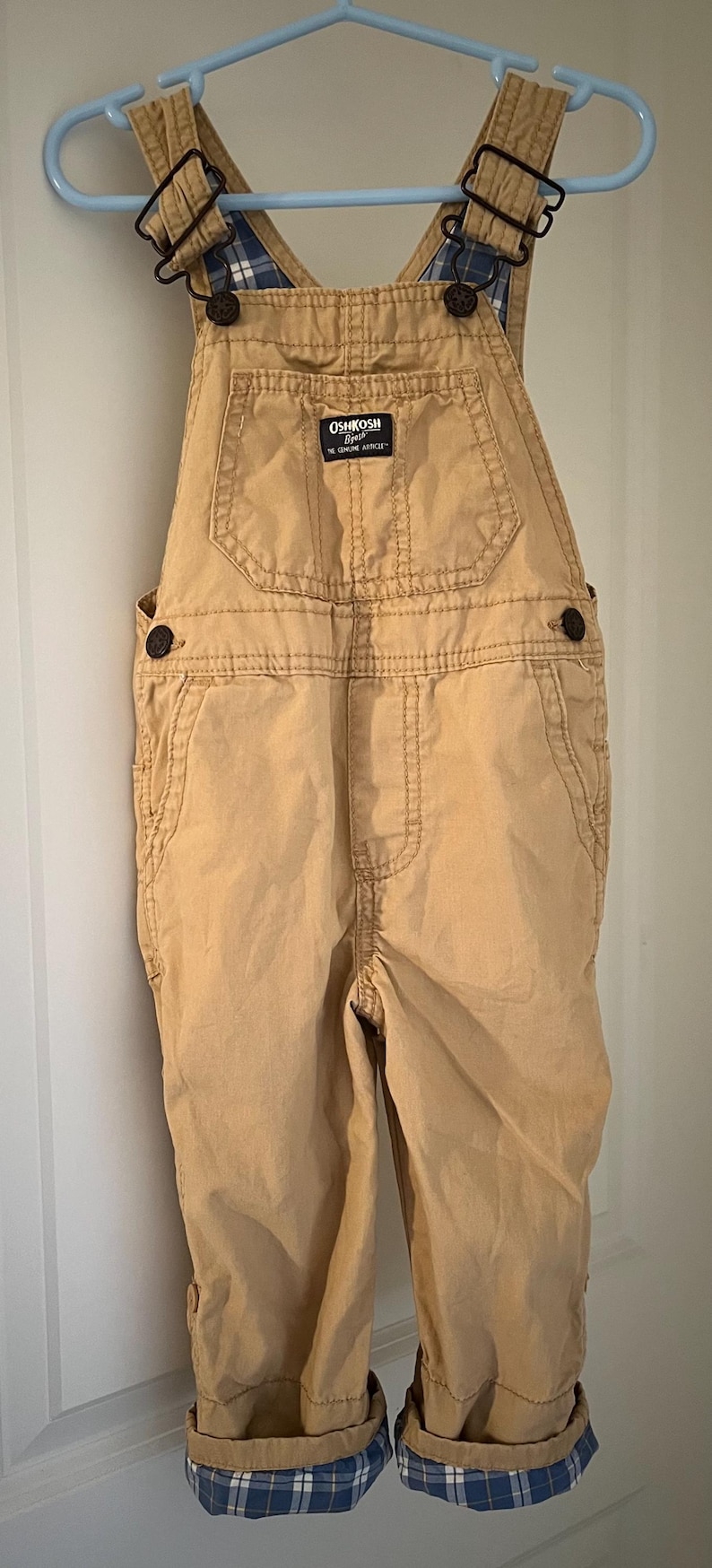 Puede incluir: Pantal&oacute;n vaquero de color beige con forro de cuadros azules y blancos en las tirantes y los pu&ntilde;os. El pantal&oacute;n vaquero tiene un parche en la parte delantera que dice "OshKosh B'Gosh The Genuine Article".