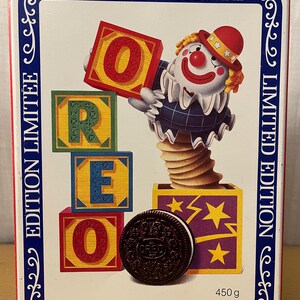 Op de afbeelding: Een blauwe en witte blikken doos met een clown die een rood, geel en groen blokje vasthoudt dat "OREO" spelt. De doos is versierd met een blauwe rand en de tekst "40th Anniversary Limited Edition" en "40e Anniversaire 450g".
