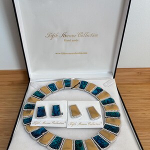 May include: A Fifth Avenue Collection jewelry set in a black box. The set includes a necklace and two pairs of earrings. The necklace and earrings feature gold and teal accents. The box is open, revealing the jewelry on a white satin interior.