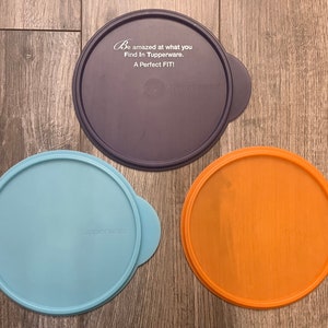 May include: Three round plastic lids in different colors: blue, orange, and purple. The purple lid has the text "Be amazed at what you Find in Tupperware. A Perfect FIT!" printed on it.